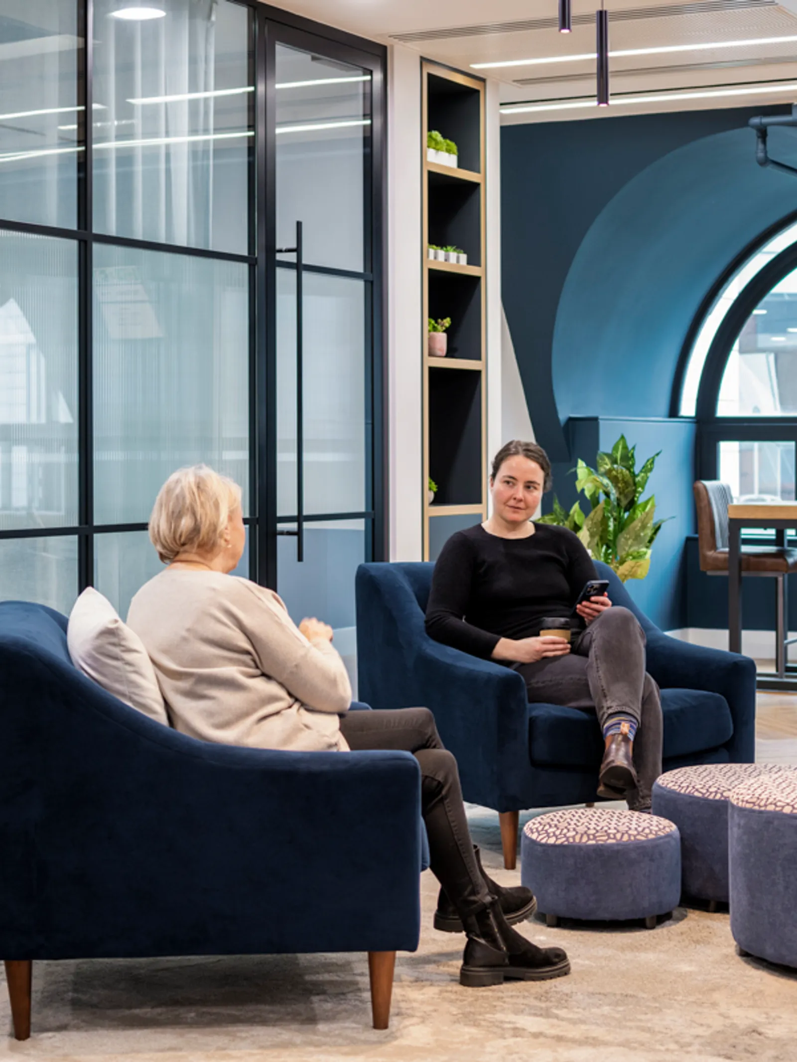 a communal hybrid office area with two people sitting on chairs talking